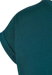 Close-up van een teal gekleurde shirt met korte mouwen, met de opgevouwen zoom en de stofstructuur zichtbaar op de mouw- en schouderpartij.