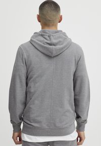 Grijze hoodie gemaakt van een zachte, gestructureerde stof. Heeft een grote capuchon, ribgebreide manchetten en onderrand, met een centrale naaddetail aan de achterkant.