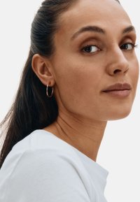 Gold hoop earrings shown worn on a model. The earrings are medium-sized with a smooth, reflective surface. The background is plain white.