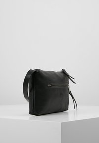 Borsa in pelle nera con una texture morbida, forma rettangolare, chiusura a zip e una tracolla laterale. Presenta una tasca con zip sulla parte anteriore.