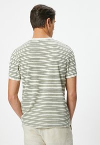 Kortærmet t-shirt i lys beige med mørkegrønne vandrette striber, med en rund halsudskæring og et blødt, struktureret stof.