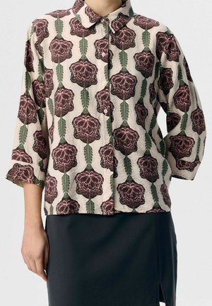 Beige button-up shirt with dark pink floral and green leaf vertical patterns, worn with black knee-length skirt. Shirt sleeves are three-quarter length.