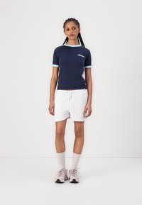 T-shirt navy a maniche corte con dettagli azzurri, abbinato a pantaloni corti bianchi. La calzatura è composta da sneakers rosa chiaro e calzini bianchi a tube.