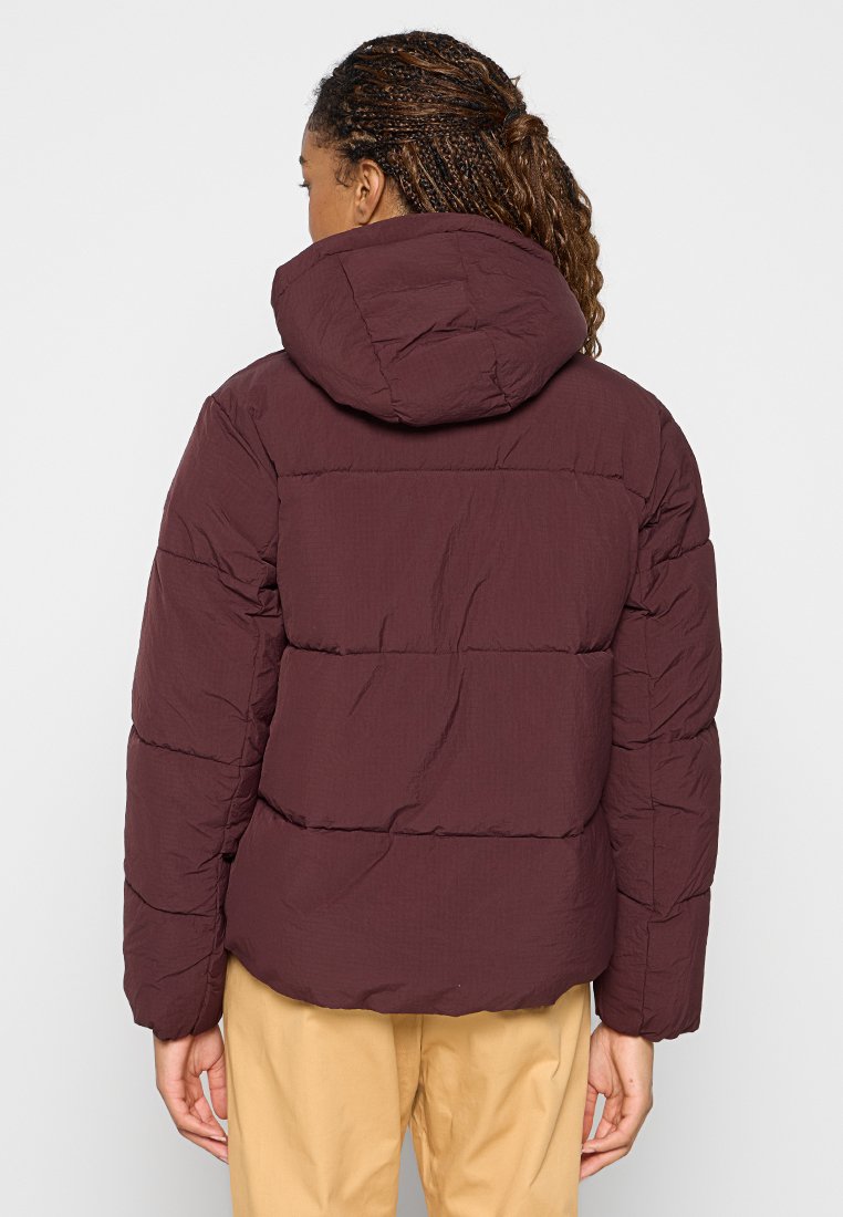 Giacca a vento bordeaux con cappuccio, caratterizzata da un'imbottitura orizzontale e una superficie liscia. Il design include una lunghezza leggermente accorciata e maniche lunghe.