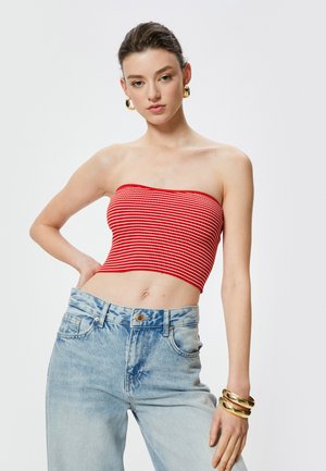 Top bandeau a righe rosse e bianche abbinato a jeans a vita alta di un blu chiaro. Braccialetti rigidi dorati e grandi orecchini sono indossati come accessori.