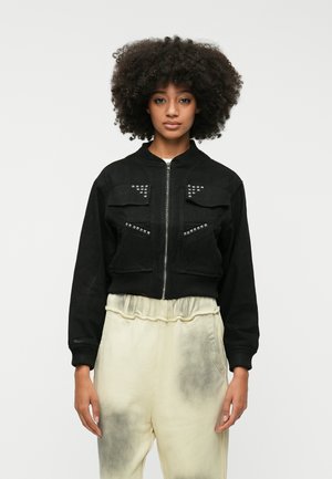 Casaco bomber preto cropped feito de tecido suave, com dois bolsos no peito, tachas prateadas nos bolsos e punhos canelados.