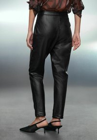 Mustad nahkpüksid, millel on kohandatud istuvus, sujuva tekstuuri ja kerge sära, koos mustade slingback-kontsadega.