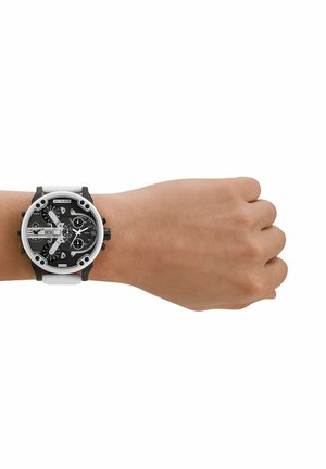 Poignet avec une grande montre ronde Diesel présentant un cadran multi-compteurs noir et blanc et un bracelet blanc sur un poignet à la peau claire.