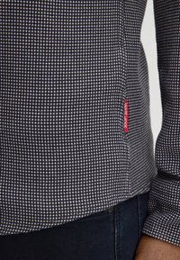 Marineblauwe en witte geruite overhemd van katoen, met een afgeronde zoom, knoopmanchetten en een rode merklabel aan de zijkant.