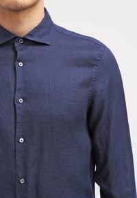 Mörkblå skjorta i linne med knapp-up design, med krage och slät textur, framhävd av kontrasterande silverknappar.
