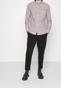 Košile na knoflíky v červeném a modrém kostkovaném vzoru, dlouhé rukávy a klasický límeček. Kombinováno s černými kalhotami a nazouvacími botami.