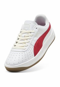 Sneakers bianchi con una striscia rossa laterale, punta forata e lacci color crema. Presentano una tomaia testurizzata e una suola in gomma marrone.