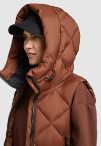 Braune gesteppte Pufferjacke mit großer Kapuze, ausgestattet mit einem Reißverschluss und schwarzen Akzenten. Kapuze gefüttert mit kontrastfarbigem Stoff.