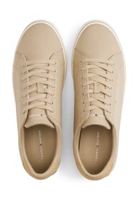 Paire de baskets beige en toile Tommy Hilfiger avec lacets et semelles blanches vues de dessus sur fond blanc.