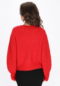 Roter gestrickter Pullover mit cropped Design, gerippter Textur und langen, weiten Ärmeln. Rückansicht, die eine lockere Passform zeigt.