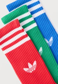 Κόκκινες, πράσινες και μπλε ριμπ αθλητικές κάλτσες με λευκές ρίγες κοντά στην κορυφή και μικρό λευκό λογότυπο Adidas σε κάθε κάλτσα.