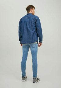 Chaqueta de mezclilla en azul oscuro, con puños abotonados y un corte relajado, combinada con jeans skinny en azul claro y zapatillas grises.