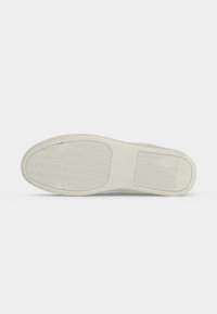 Semelle d'une chaussure blanche avec des motifs texturés antidérapants sur un fond clair uni.