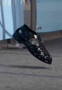 Μαύρο σανδάλι από πολυουρεθάνη με πλεκτό σχέδιο, ανοιχτή μύτη, ρυθμιζόμενο λουράκι με αγκράφα και στιβαρή επίπεδη σόλα.