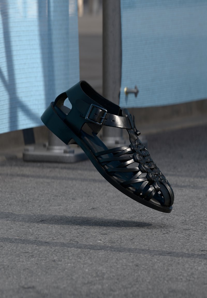 Μαύρο σανδάλι από πολυουρεθάνη με πλεκτό σχέδιο, ανοιχτή μύτη, ρυθμιζόμενο λουράκι με αγκράφα και στιβαρή επίπεδη σόλα.