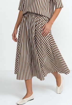 Person wearing a brown and white vertical striped skirt with a matching top and white perforated flat shoes, mid-step against a white background.