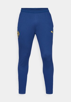 Blauwe sportbroek van soepele stof, met een geel embleem en een klein gouden Puma-logo op het linkerbeen, met een taps toelopend ontwerp.