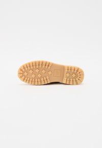 Semelle de chaussure en caoutchouc brun clair avec un motif texturé et des rainures profondes pour une bonne adhérence ; présente un logo carré embossé au centre.