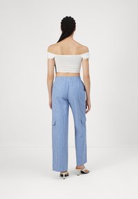Dryžuotos mėlynos krovinių kelnės su elastine juosta ir šoninėmis ki�šenėmis, derintos su baltu off-shoulder trumpu topu ir juodais aukštakulniais sandalais.