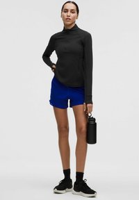 Musta pika varrukaga spordipluus, sinised lühikesed püksid, mustad spordijalatsid, hoiab musta joogipudelit. Sile kangas, vormiv disain, lõdva spordiriietus.