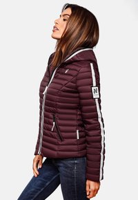Giacca a vento bordeaux con texture a cucitura verticale, zip bianca, tasche laterali e un'etichetta logo sulla manica. Design con cappuccio.