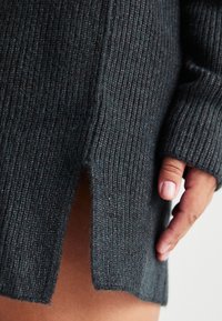 Gray ribbed sweater with a side slit, showing a soft texture and a fitted design. Hand placed near the slit for detail.