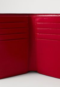 Interno di un portafoglio in pelle rossa con più slot per carte, texture liscia e bordi cuciti. Nome del marchio impresso in un angolo.