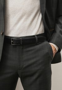 Tummakuviollinen puku, jossa on tekstuuri, yhdistettynä vaaleanbeigeen neuleeseen ja mustaan nahkavyöhön, jossa on hopeinen solki.
