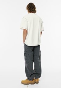 Witte katoenen t-shirt met korte mouwen, gecombineerd met donkergrijze cargobroek met meerdere zakken, en tan kleurige veterschoenen.