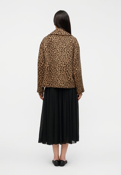 Μπουφάν με λεοπάρ σχέδιο και απαλή υφή, διαθέτει γιακά και κουτί σχήμα, σε συνδυασμό με μαύρη πλισέ φούστα και ίσια παπούτσια.