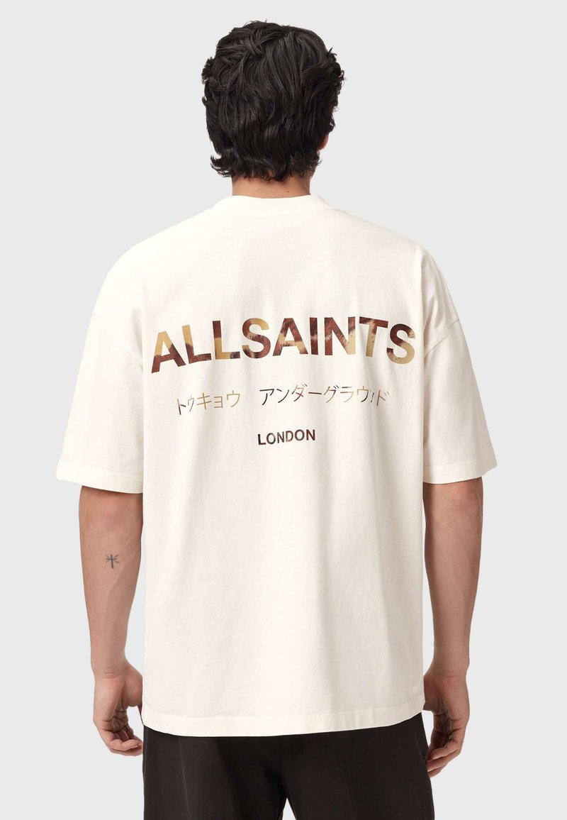 Μπεζ βαμβακερό t-shirt με μεγάλο κείμενο "ALLSAINTS" σε σκούρο καφέ και χρυσό στην πλάτη, με επιπλέον κείμενο στα ιαπωνικά και τη λέξη "LONDON" από κάτω.