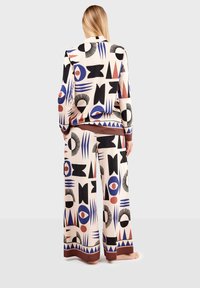 Two-piece outfit featuring a cream base with abstract black, blue, and red geometric patterns. Fabric appears smooth; pants have wide legs.