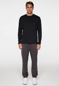 Musta pitkähihainen paita, jossa pyöreä pääntie, yhdistetty harmaisiin collegehousuihin, joissa on rento istuvuus ja joustava vyötärönauha. Valkoiset tennarit täydentävät asun.