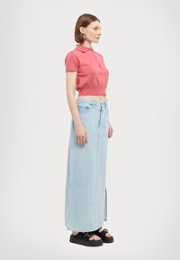 Lys rosa kortermet polo skjorte, kombinert med en lys blå denim maxiskjørt med sidespalter og svarte platå sandaler.