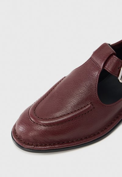 Καφέ δερμάτινο παπούτσι με στρογγυλεμένη μύτη, πλαϊνές κοψιές και λουράκι με ασημένια αγκράφα. Υφή επιφάνειας και αντίθετη ραφή. Μαλακή εσωτερική επένδυση.