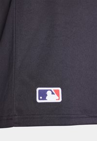 Tela negra con textura suave, que presenta un parche bordado del logo de la MLB en blanco con acentos rojos y azules en la esquina inferior.