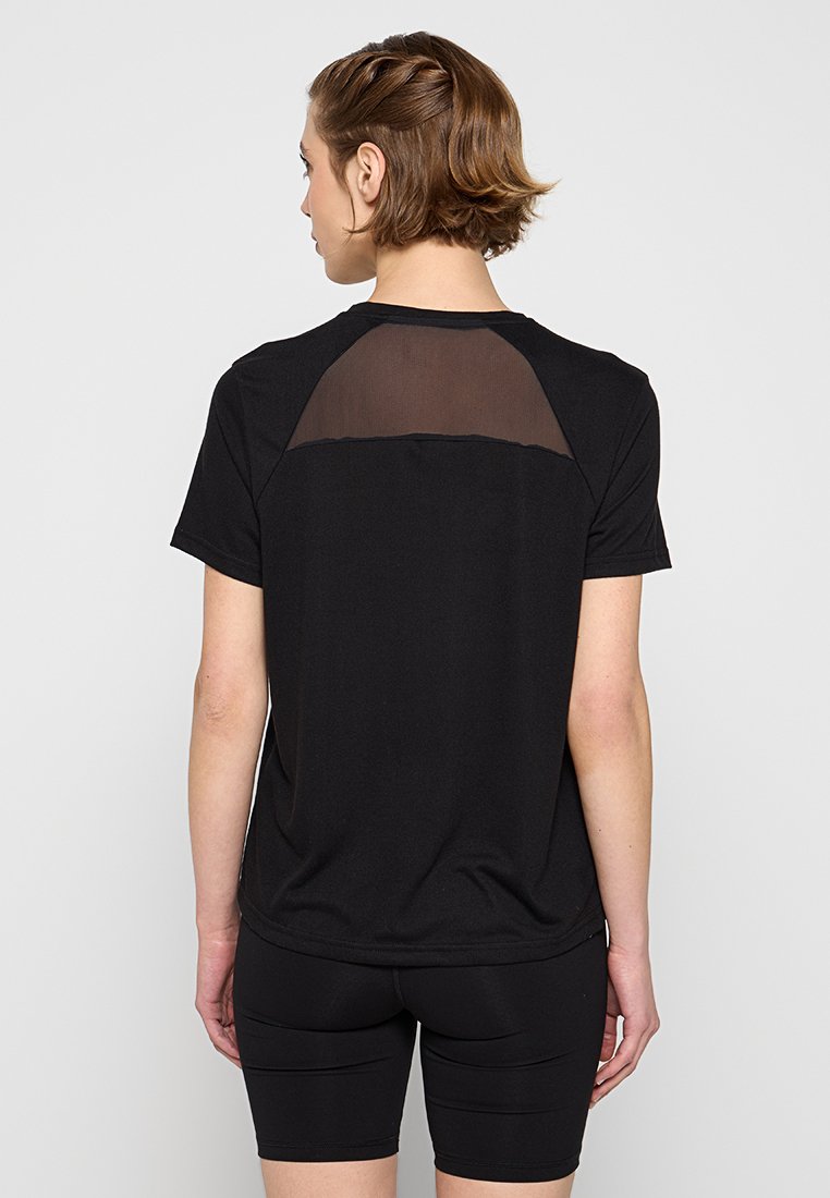 Mujer con cabello corto castaño, vistiendo una camiseta negra de manga corta con un panel de malla transparente en la parte superior de la espalda y pantalones cortos de ciclismo negros.