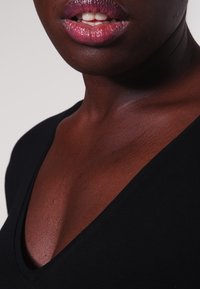 Top nero a V con una superficie liscia, che mette in risalto un collo color carne e un'area della clavicola scoperta, enfatizzando il suo design aderente.