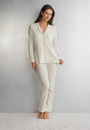 Lichtcrème geribde pyjama set bevat een button-up shirt met een zak en lange broek, gemaakt van zachte, gestructureerde stof.