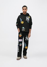 Black hoodie and joggers featuring colorful NYC-themed patches, including the Statue of Liberty and dice, with relaxed fit and kangaroo pocket.