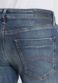 Vaqueros de mezclilla azul oscuro con corte recto, que presentan un parche de logo de cuero, costuras de cobre y un diseño clásico de bolsillo trasero.
