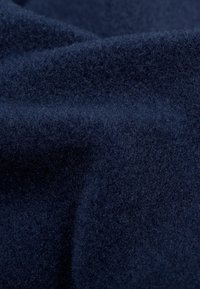 Tessuto in lana di un blu scuro, con una consistenza morbida e una superficie leggermente pelosa, che mostra sottili variazioni di colore e intrecci. Materiale denso e non riflettente.