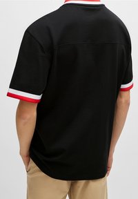 Svart kortärmad skjorta med röda och vita randiga detaljer vid kragen och ärmsluten, med en mjuk bomullstextur.