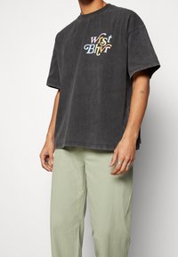 Mörkgrå oversized t-shirt med ett flerfärgat grafiskt tryck "wrist bhvr" på bröstet. Bärs med ljusgröna löst sittande byxor.