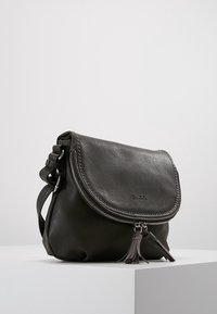 Borsa a tracolla in pelle grigia con pattina curvata, hardware in argento, chiusura con zip e una nappina decorativa. Texture liscia con una grana sottile.